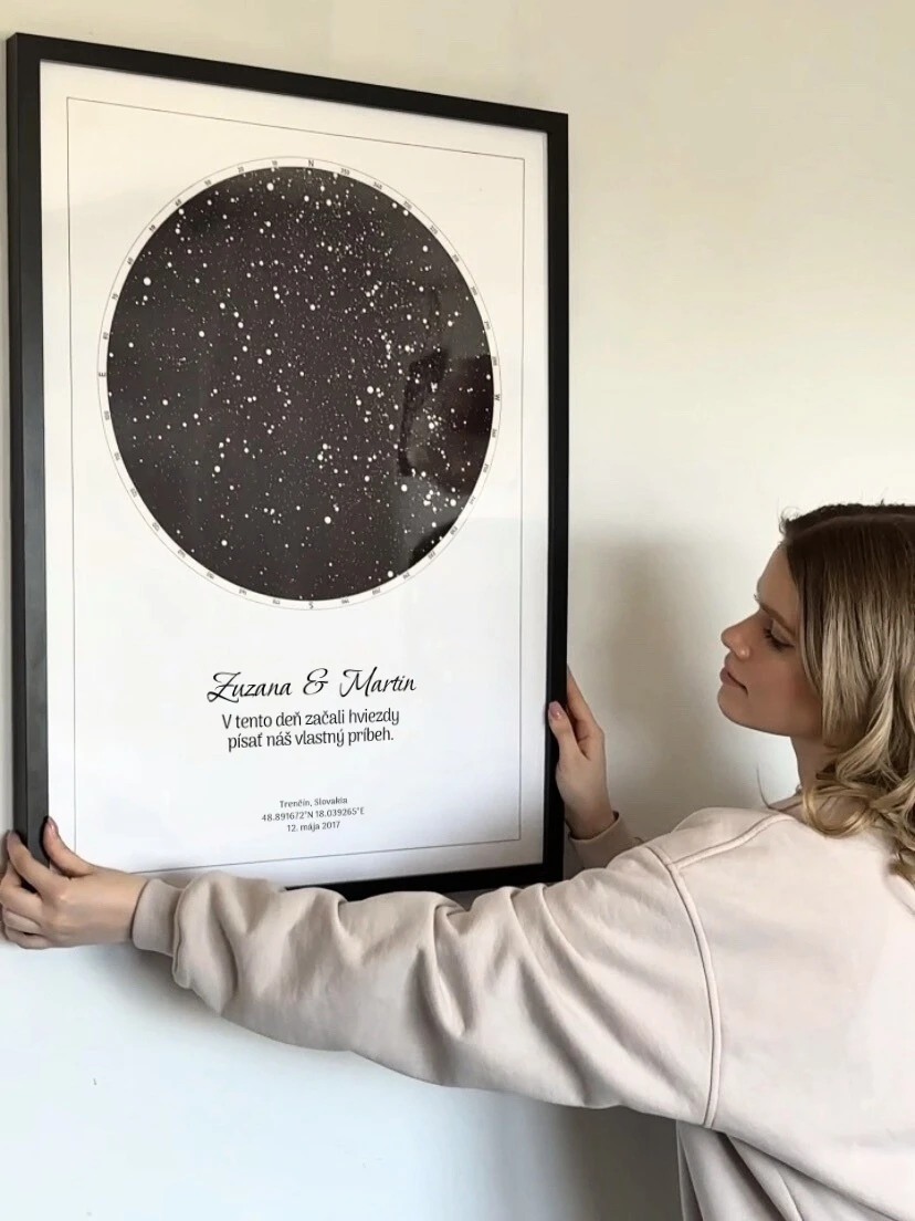 Žena drží veľký zarámovaný plagát, ktorý ukazuje reálnu veľkosť produktu. Personalizovaná hviezdna mapa a krásna hviezdna obloha.